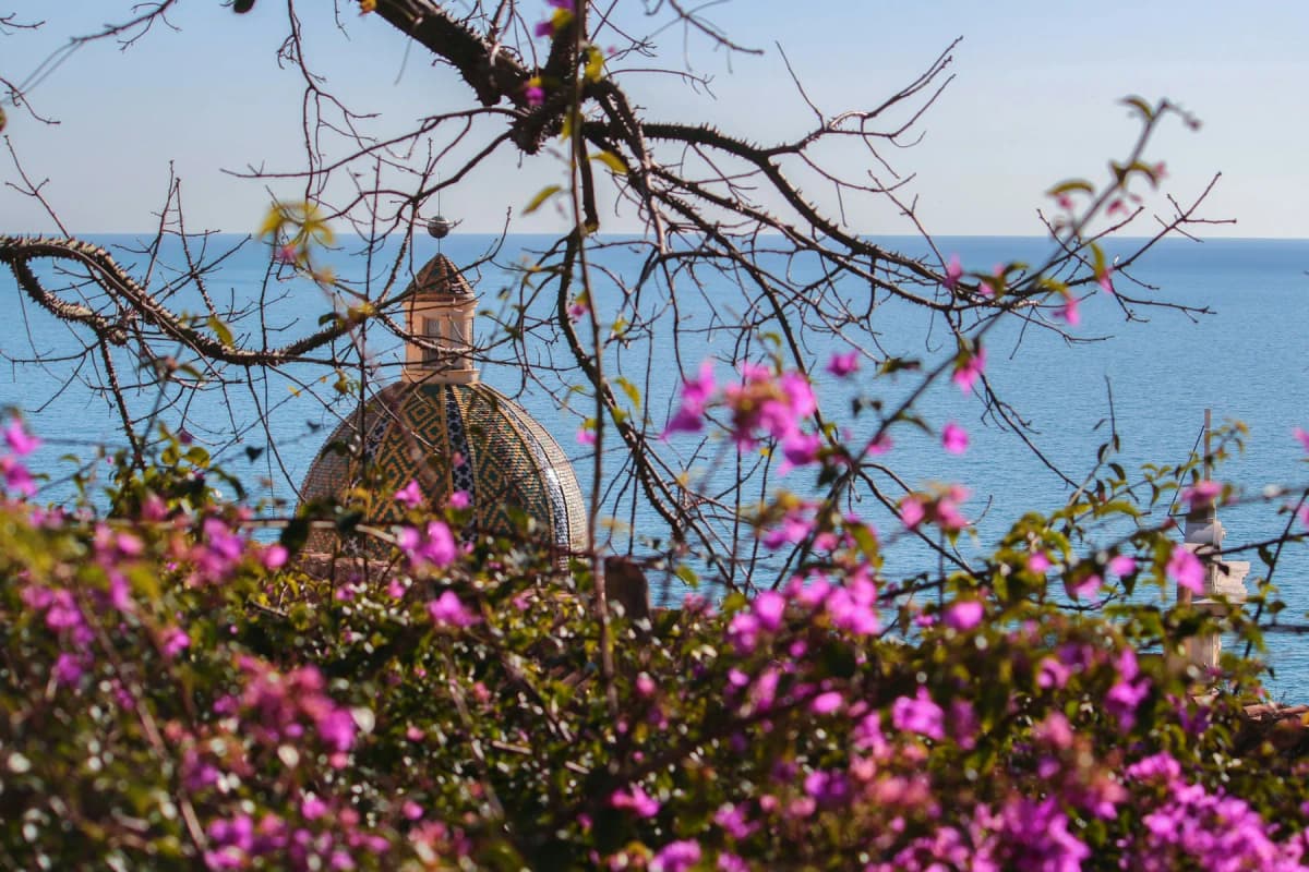 The tiled dome of Santa Maria Assunta in Positano seen through pink bougainvillea, with the sea behind