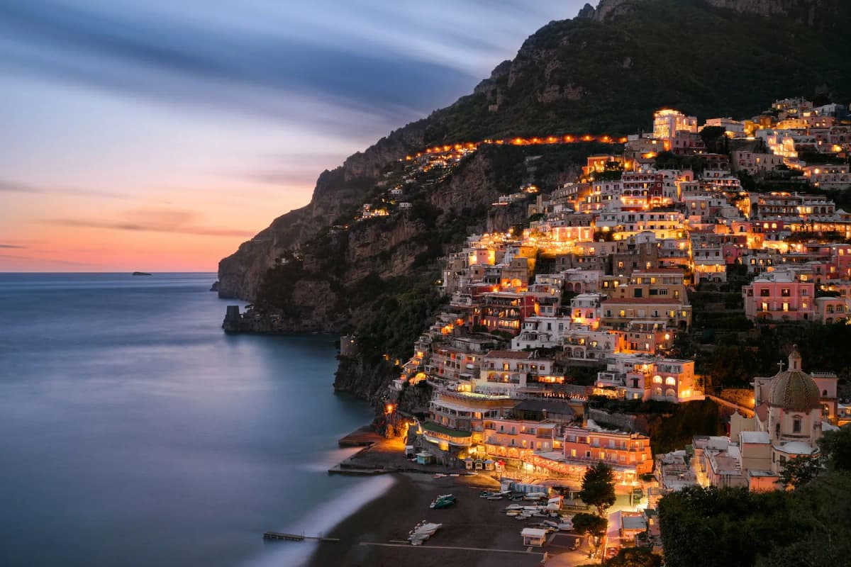 Positano lit up at dusk, with the lights of the houses reflected in the sea