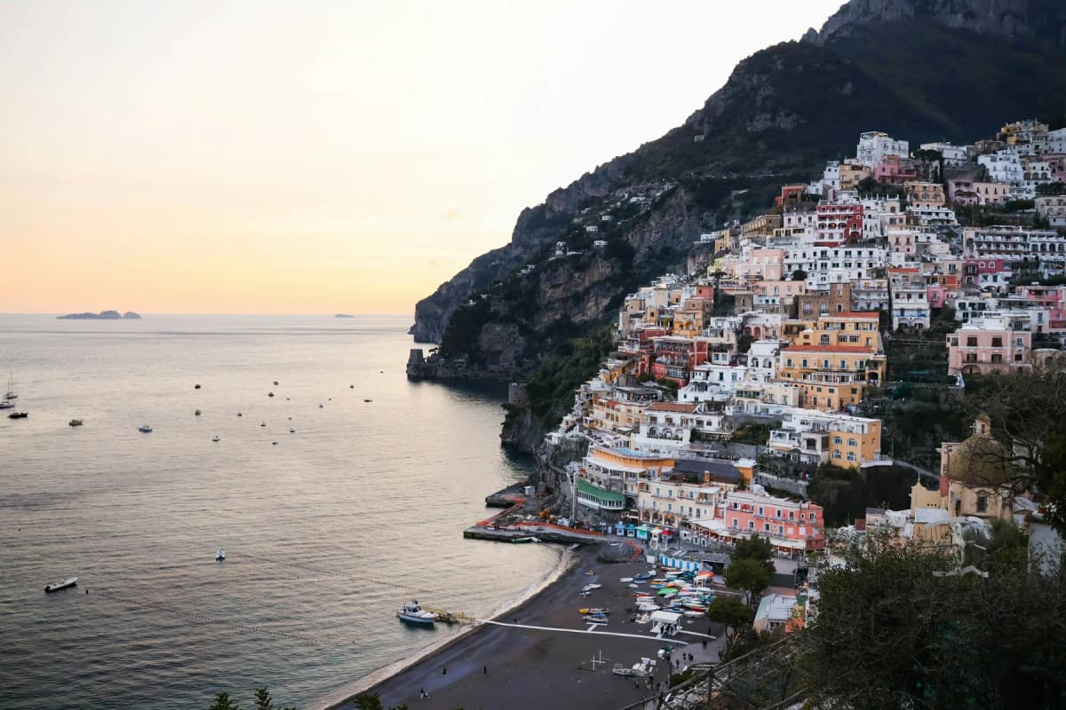 Positano at sunset seen from the road above the town, with houses stepping down the hillside to the beach