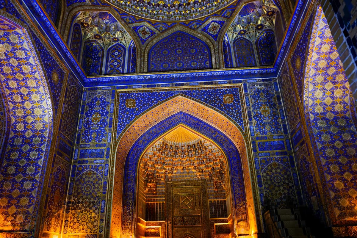 A tiled and gilded interior with deep blue walls and a golden mihrab in a madrasah on Samarkand's Registan