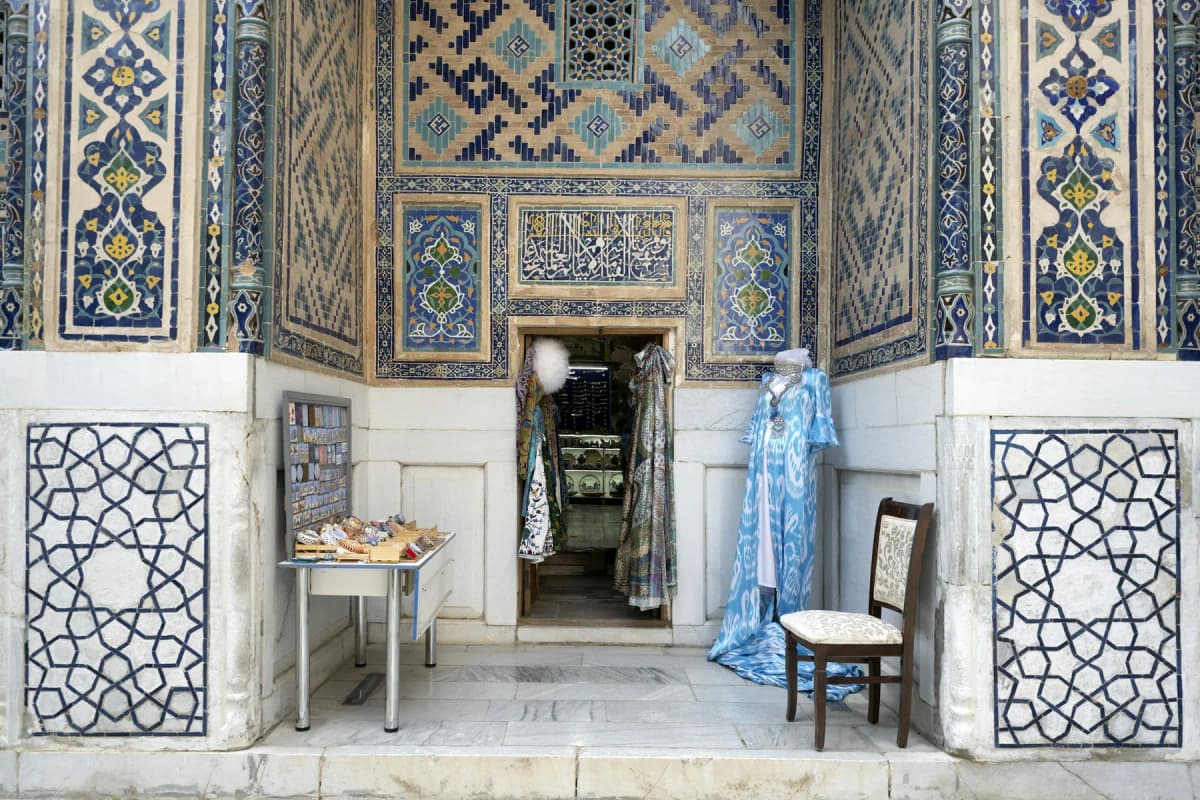 Things to do in Samarkand: a craft shop set into a tiled niche in a madrasah courtyard on the Registan, with embroidered clothes on display