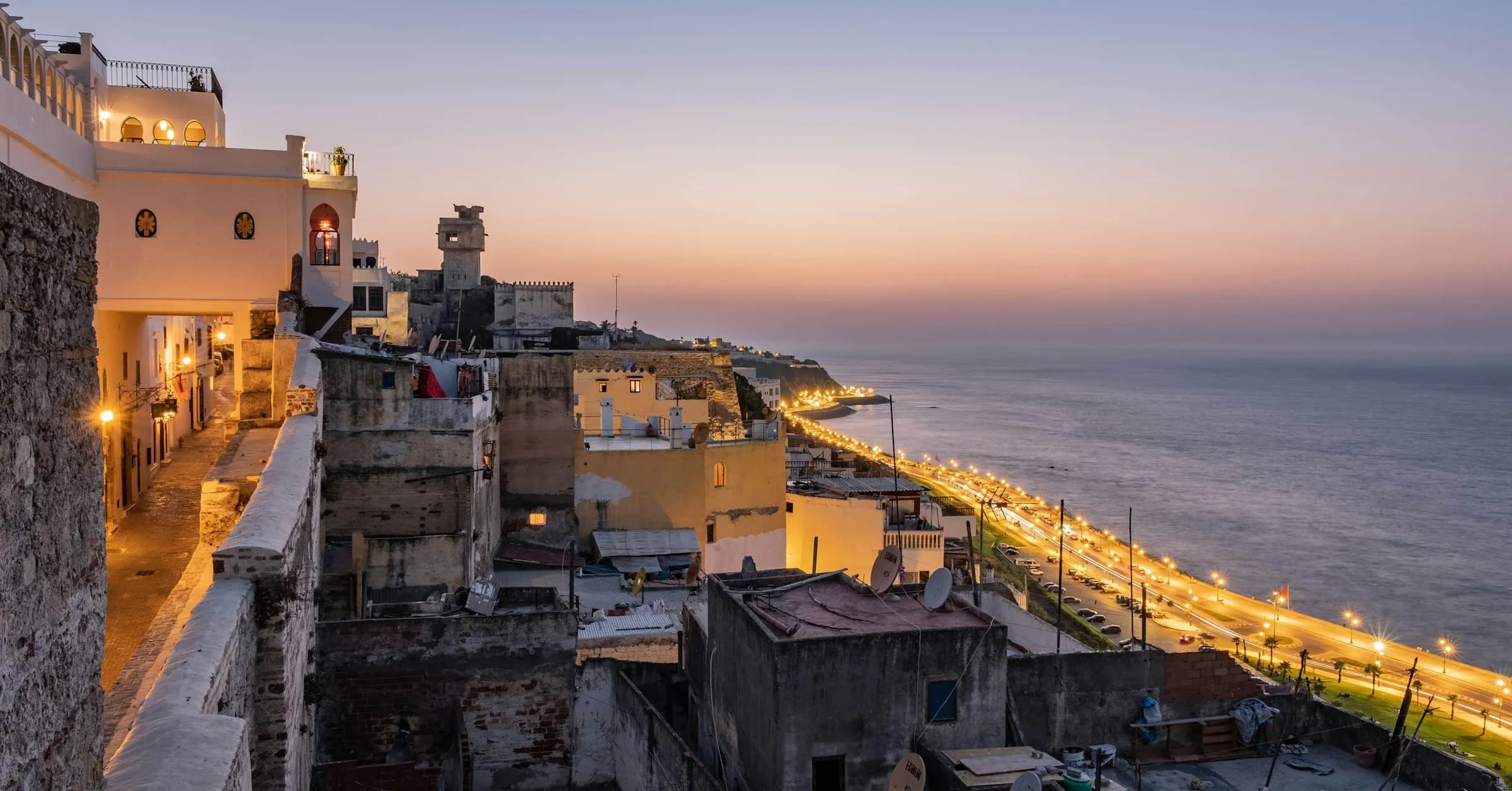 Things to do in Tangier: the white houses of the medina above the lit corniche and the Strait of Gibraltar at dusk