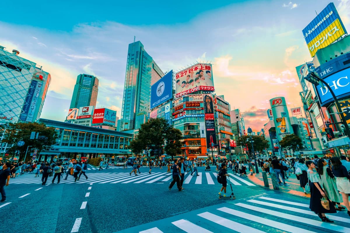 People crossing the wide zebra stripes of Shibuya scramble crossing in Tokyo in daylight
