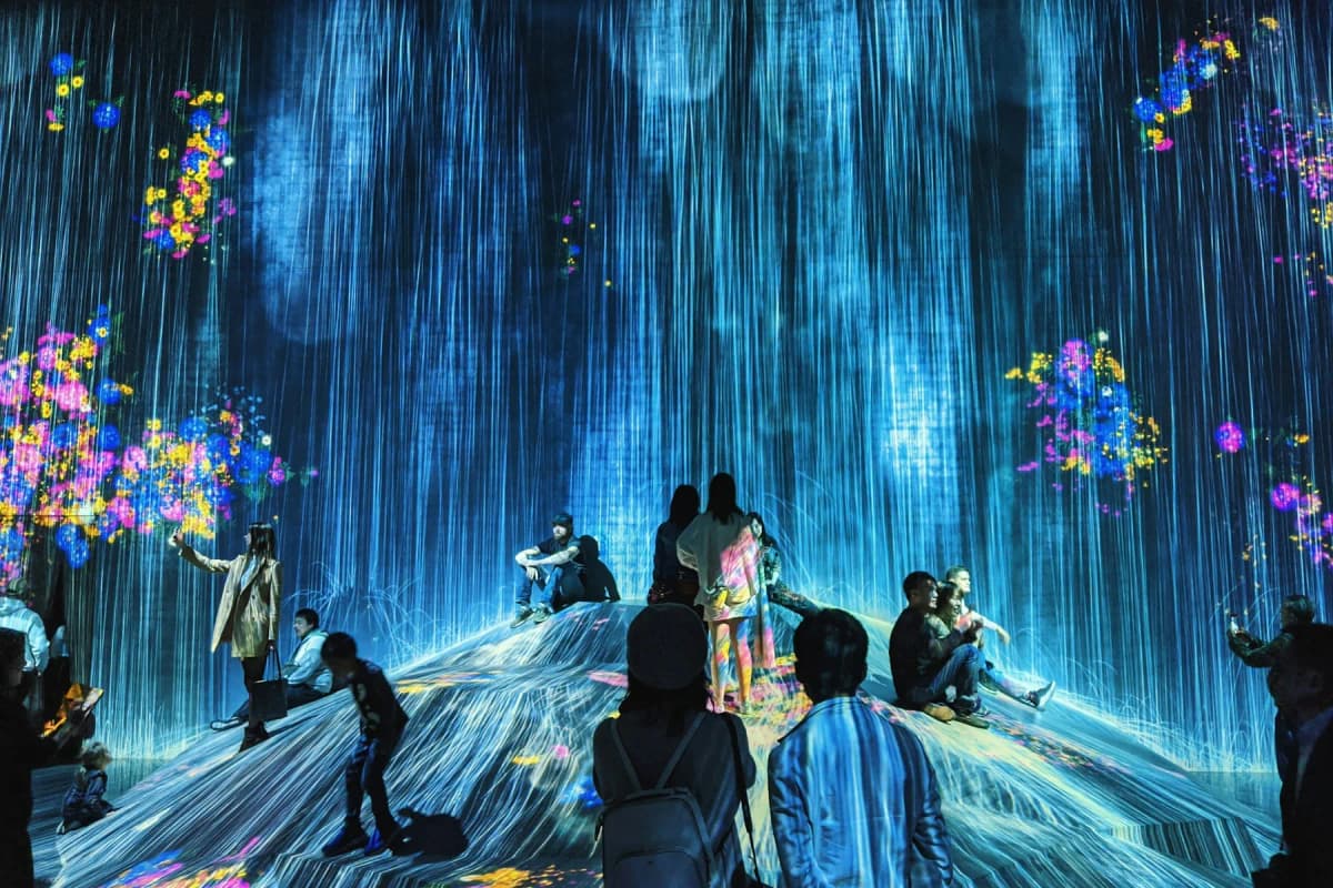 Visitors sitting inside an immersive digital art installation of falling light at teamLab in Tokyo