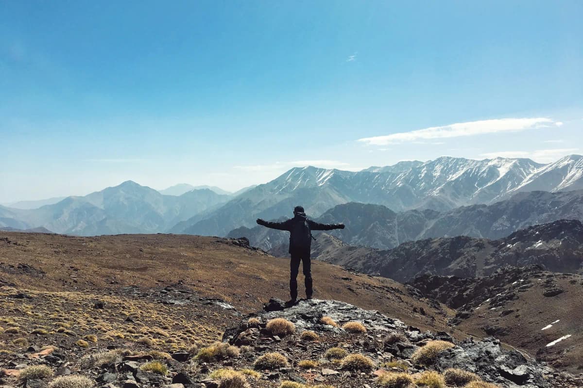 A hiker standing on a rocky ridge with the snow-capped High Atlas mountains behind