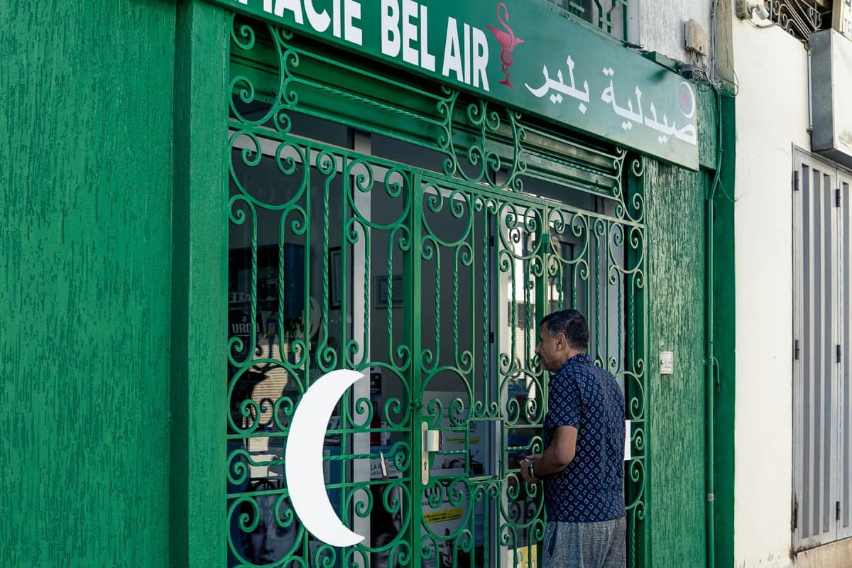A man standing at the entrance of a green-fronted pharmacy in Morocco