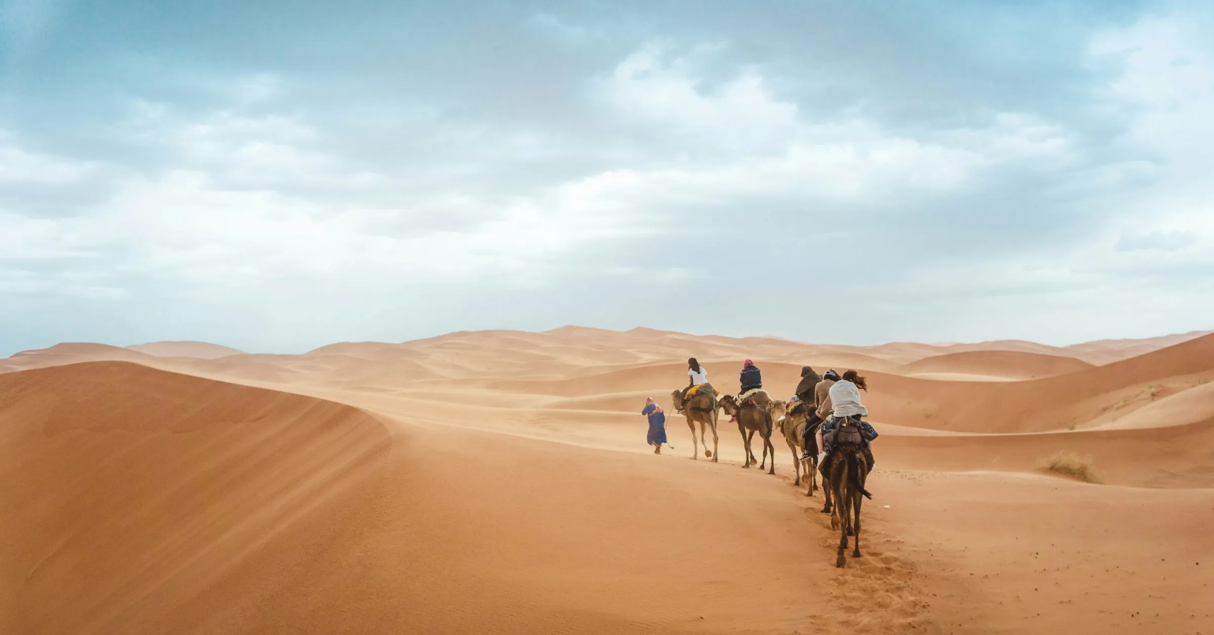 Travel insurance for Morocco: a camel caravan with riders crossing the Sahara dunes