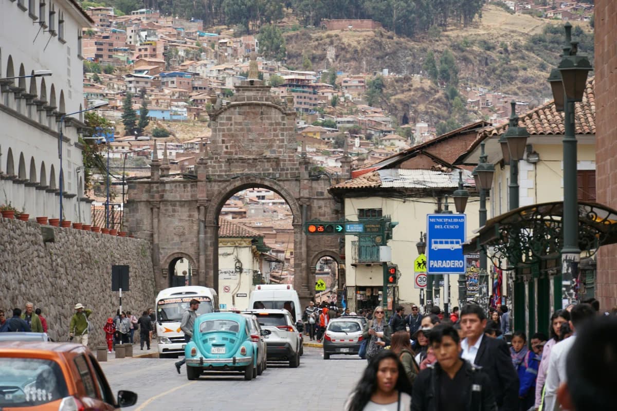 A busy street in central Cusco with people walking towards a stone arch