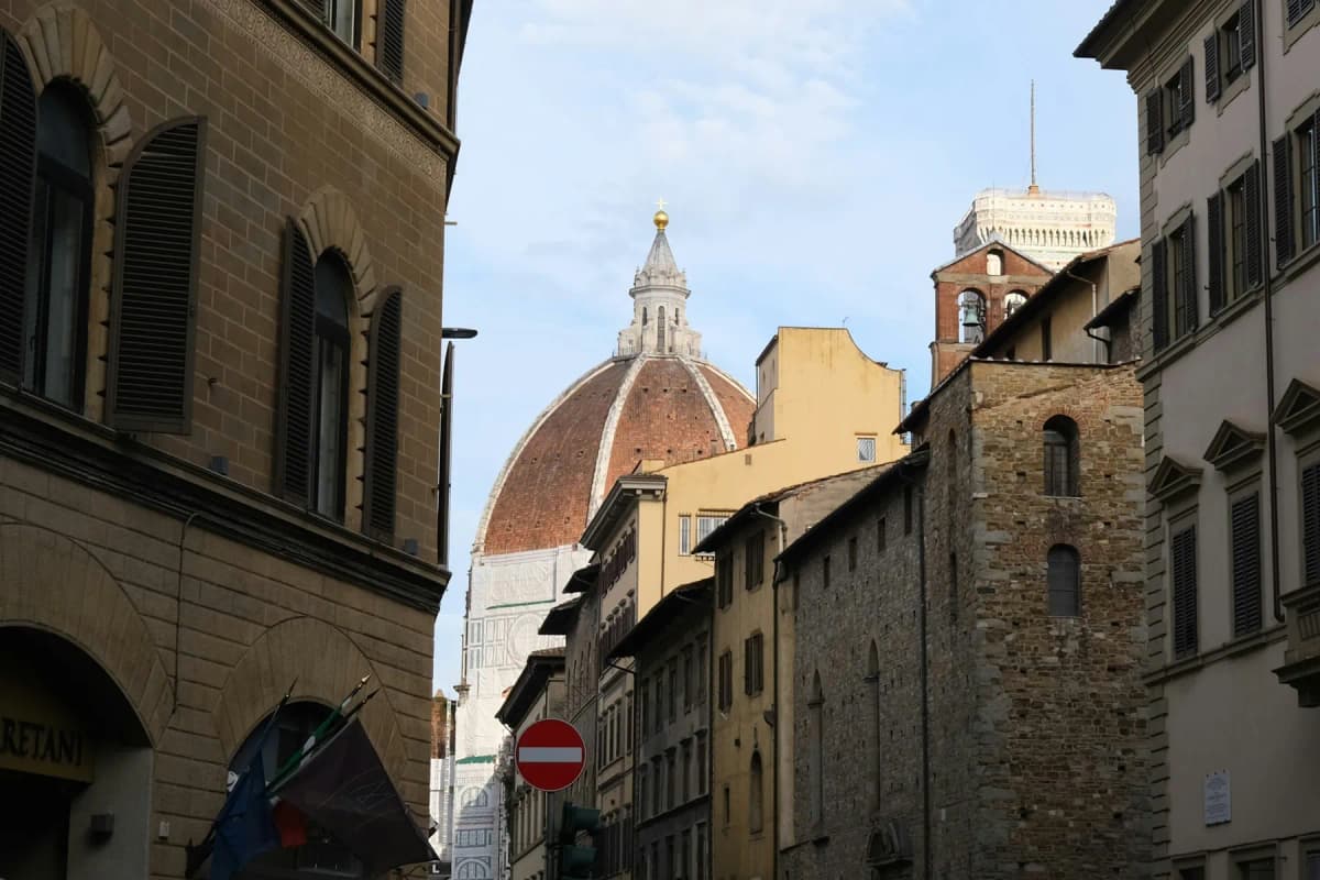 The dome of Florence cathedral seen between old stone buildings on a narrow street