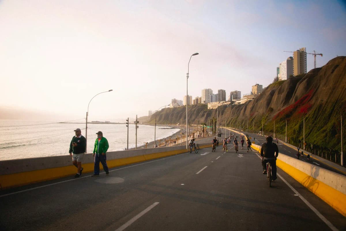 People walking and cycling on a road beside the sea below Lima's cliffs