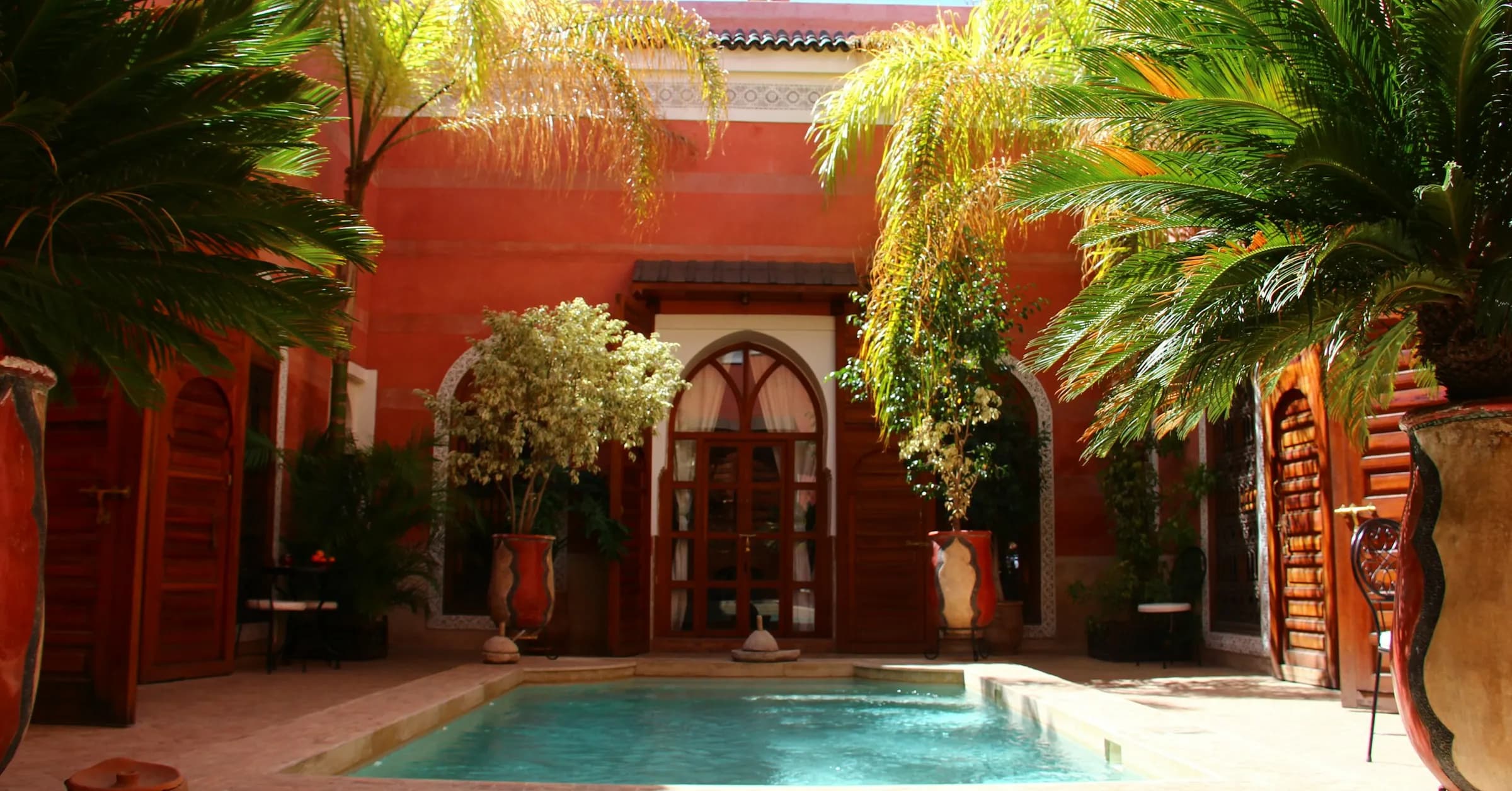 Where to stay in Marrakech: a riad courtyard with a plunge pool, palms and terracotta walls in the medina