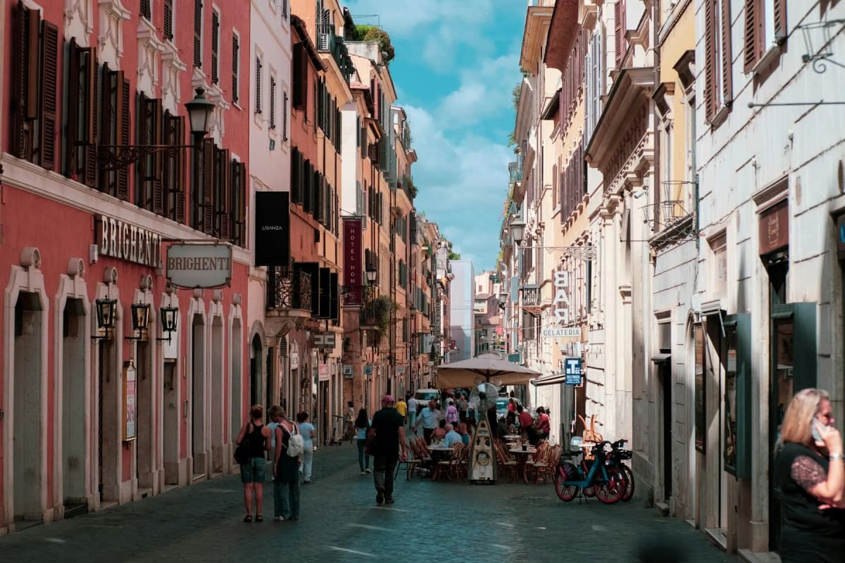 A narrow Roman street lined with ochre and terracotta buildings and cafe tables