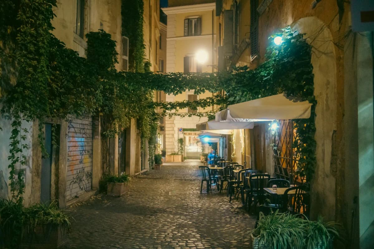 An ivy-covered cobbled lane in Trastevere at night with restaurant tables outside