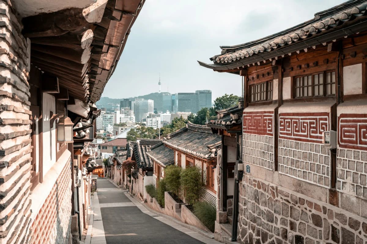 A lane of traditional hanok houses in Bukchon Hanok Village, with the city and N Seoul Tower in the distance