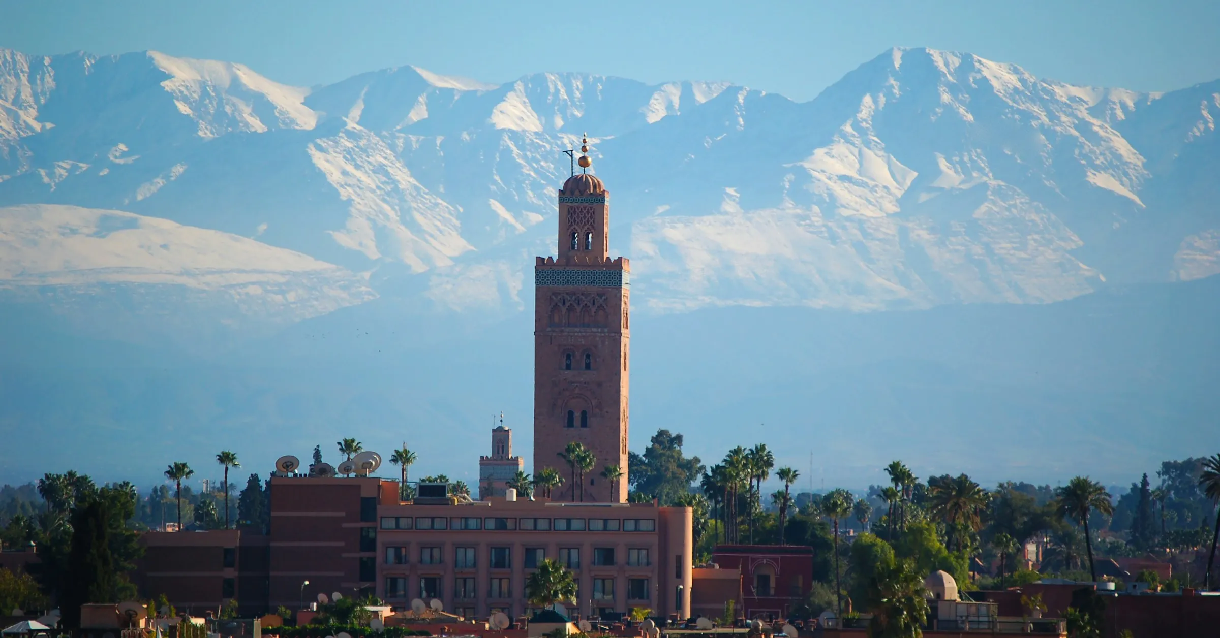 Day trips from Marrakech: the Koutoubia minaret with the snow-covered High Atlas mountains behind the city