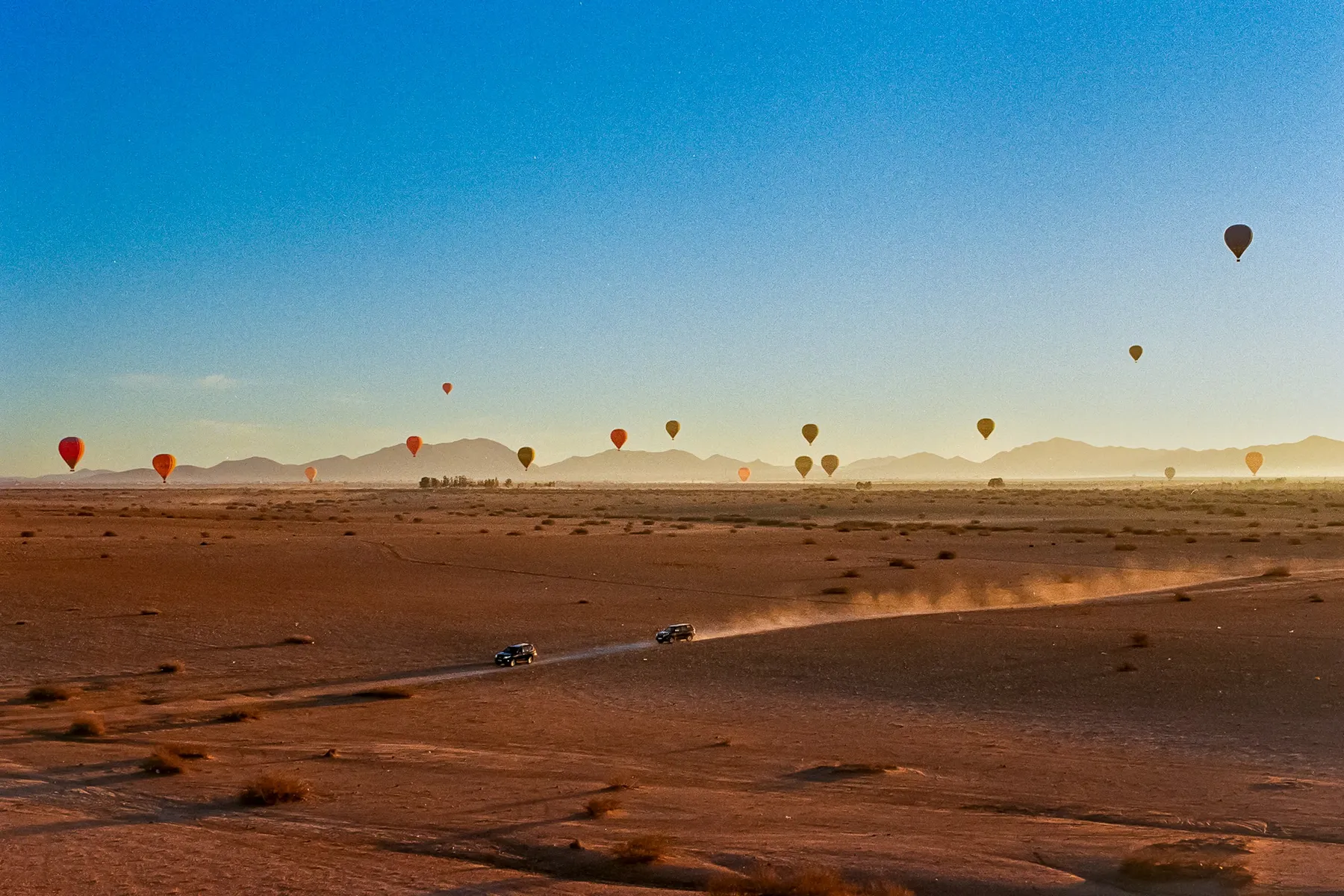 Hot-air balloons rising over the Agafay desert near Marrakech at sunrise, with the Atlas mountains behind