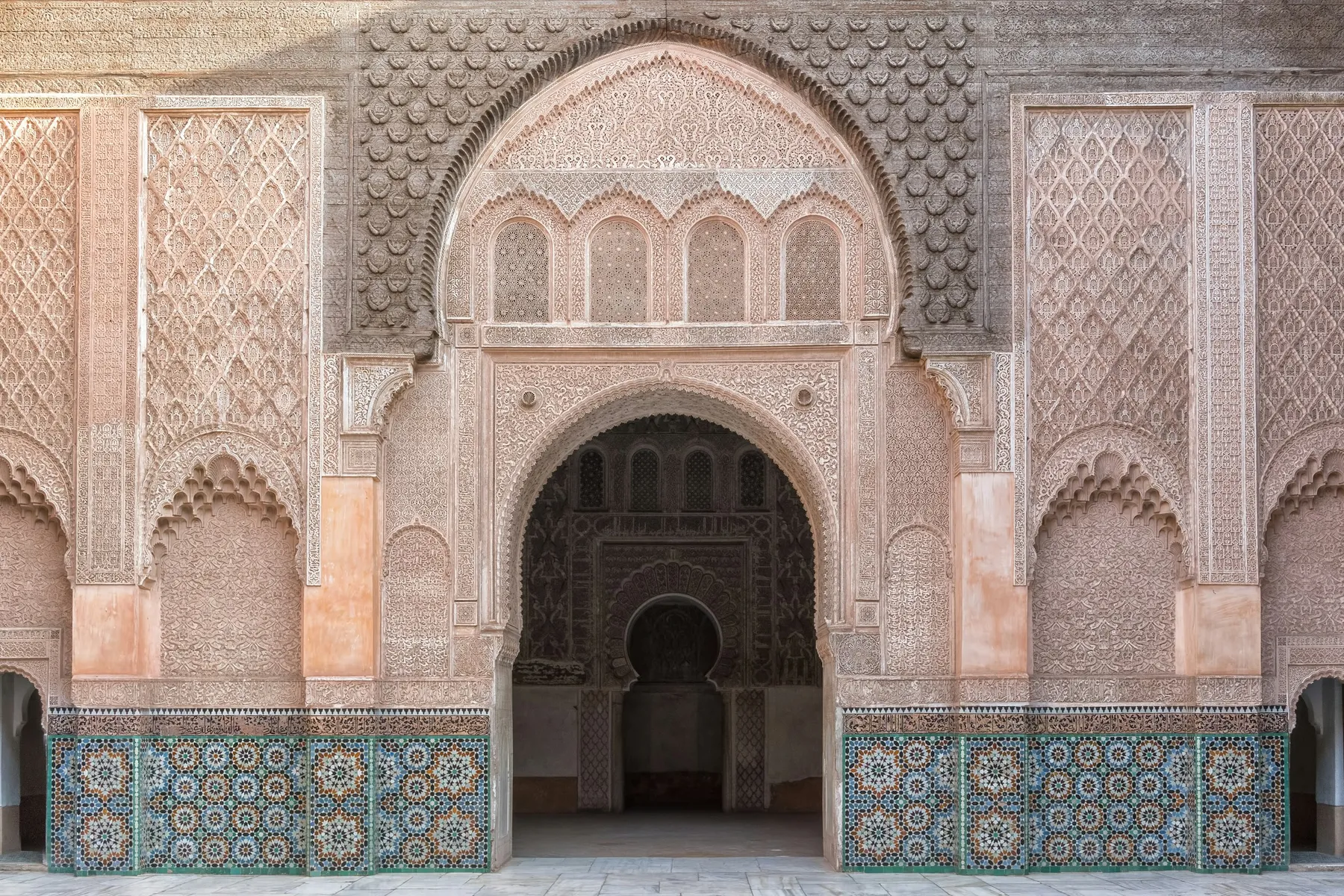 Carved stucco arch above zellige tilework in the courtyard of a Moroccan madrasa