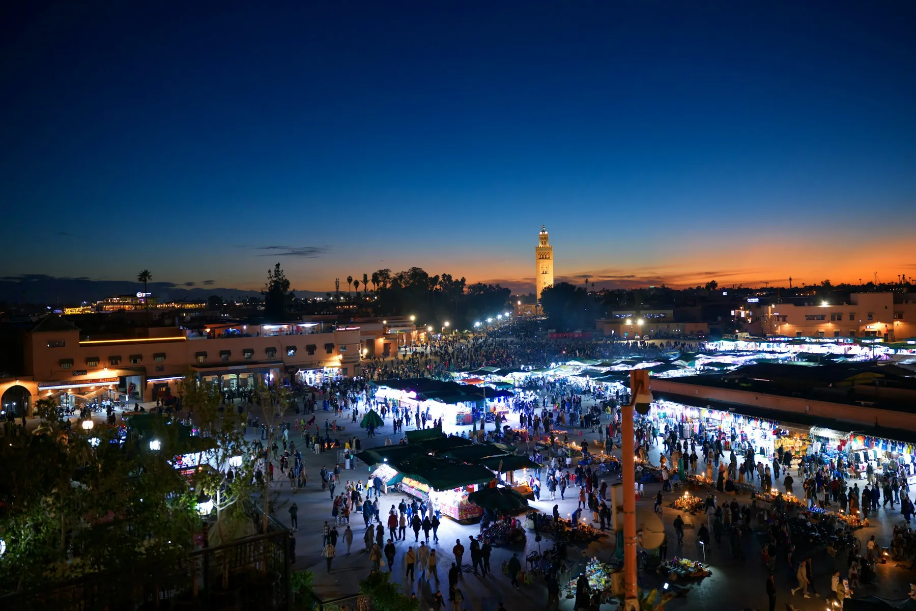 Jemaa el-Fnaa square at dusk with glowing food stalls and the Koutoubia minaret in the distance